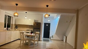 Et moderne køkken med hvide skabe, et spiseområde med bord og stole, samt en trappe til en etage ovenover.