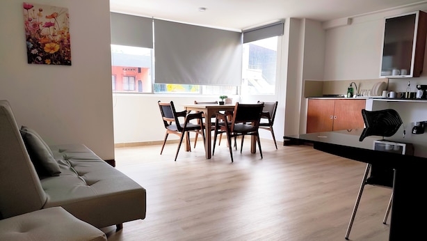 A modern living room with a sofa, dining table, and chairs. There is a kitchen area with cabinets and a countertop. - ABC-53 (Medellín)