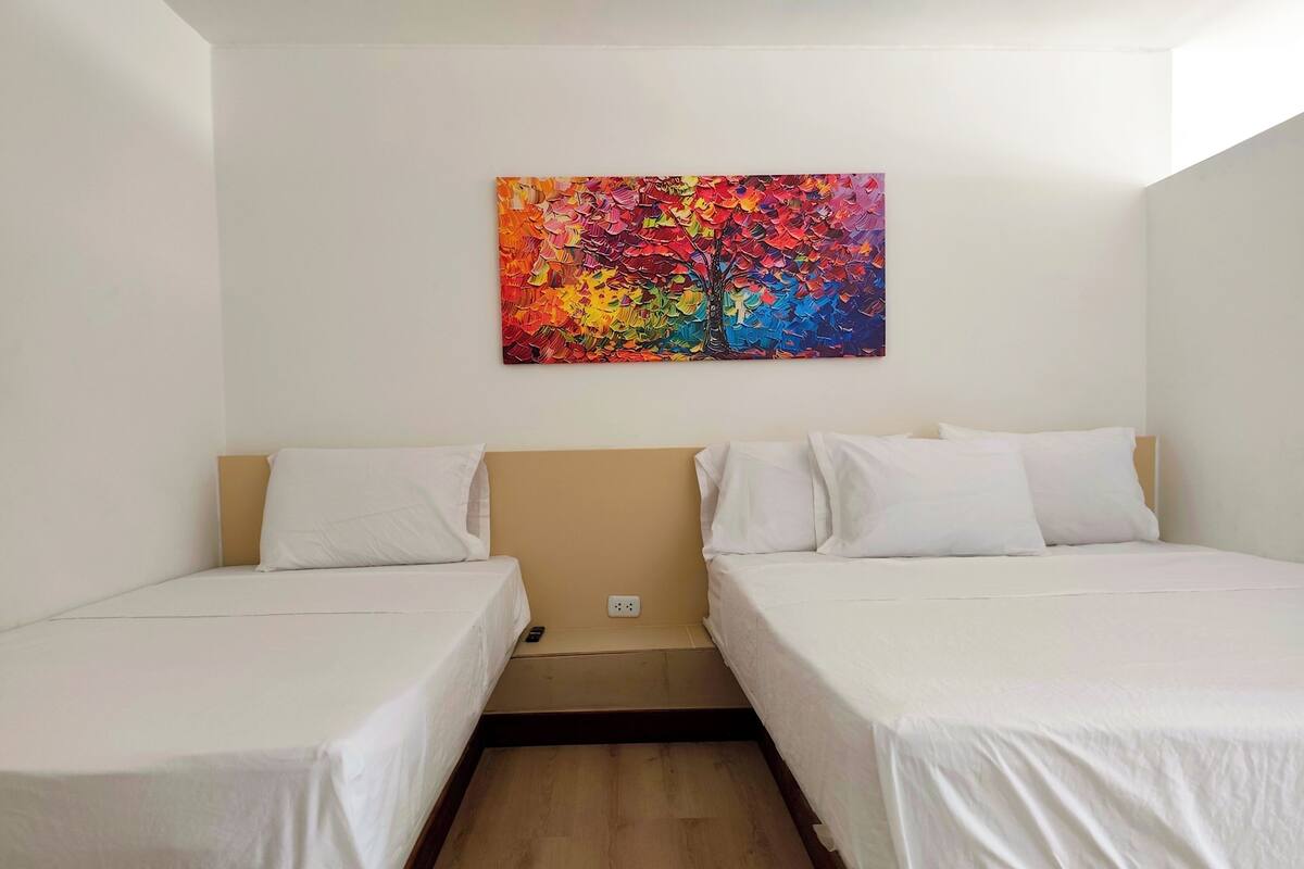 Une chambre avec deux lits simples, un plancher en bois et une peinture abstraite aux couleurs vives accrochée au mur.