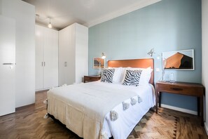 A neatly arranged bedroom with a large bed, two bedside tables, a wardrobe, and a wall-mounted lamp. - Casas da Tapada 1 In front of the wonderful Tapada das Necessidades (Lisboa)