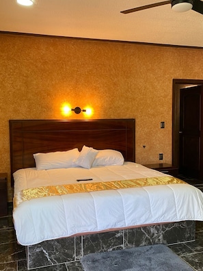 A hotel room with a large bed, a wooden headboard, a marble floor, and a ceiling fan. - Enrique Resendiz Vega (Colon)