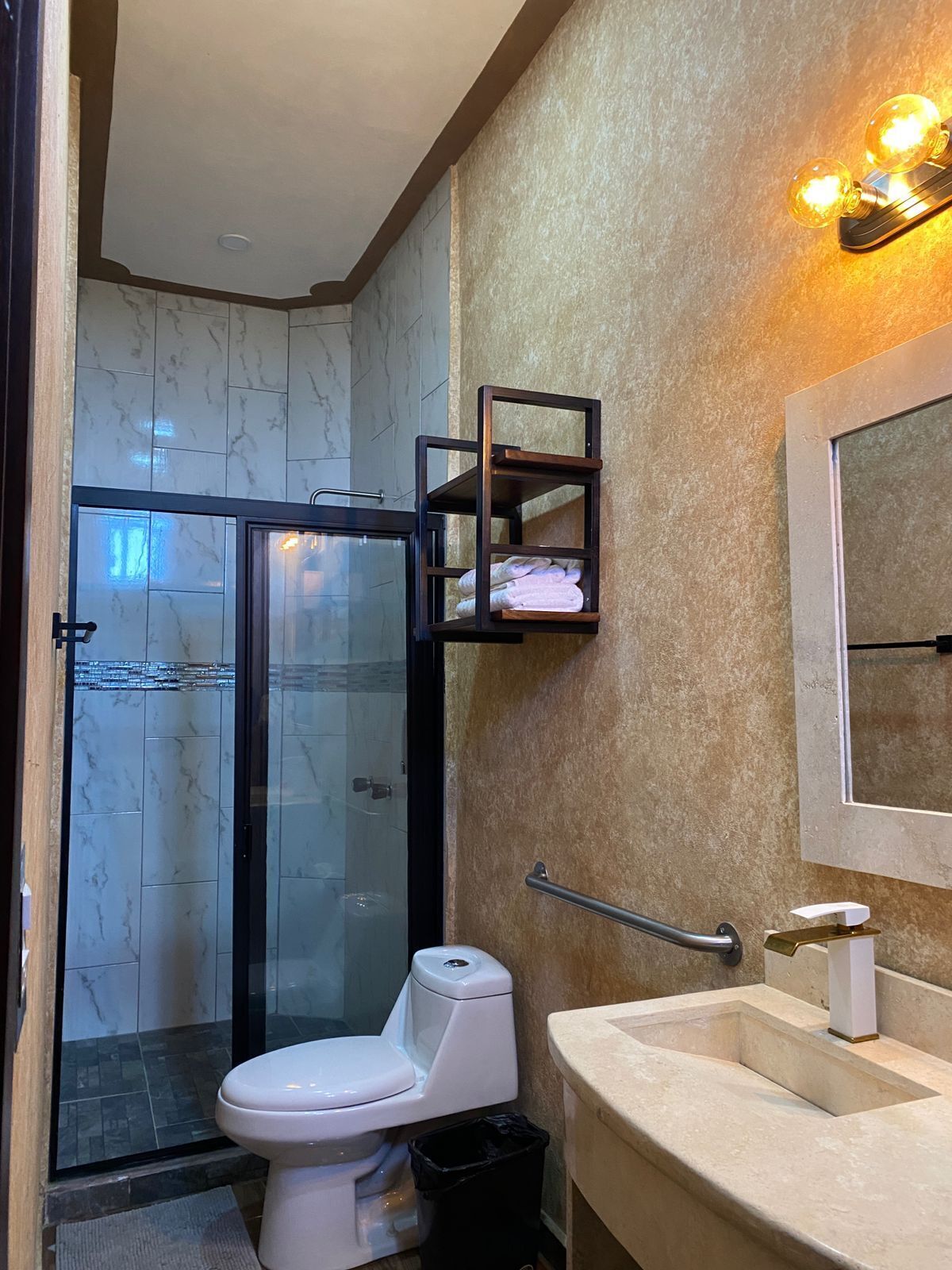 Un baño moderno con cabina de ducha de vidrio, inodoro blanco, lavabo color beige y perchero.