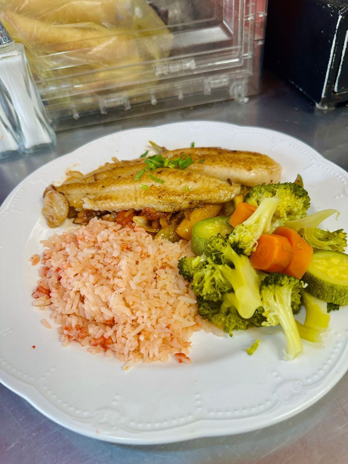 A plate of food with rice, vegetables, and a fish fillet.
