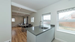 A modern kitchen with a central island, a dining area with a table and chairs, and large windows with patterned curtains. - Duplex Apartment - Modern & Convenient - Pass the Keys (Reading)