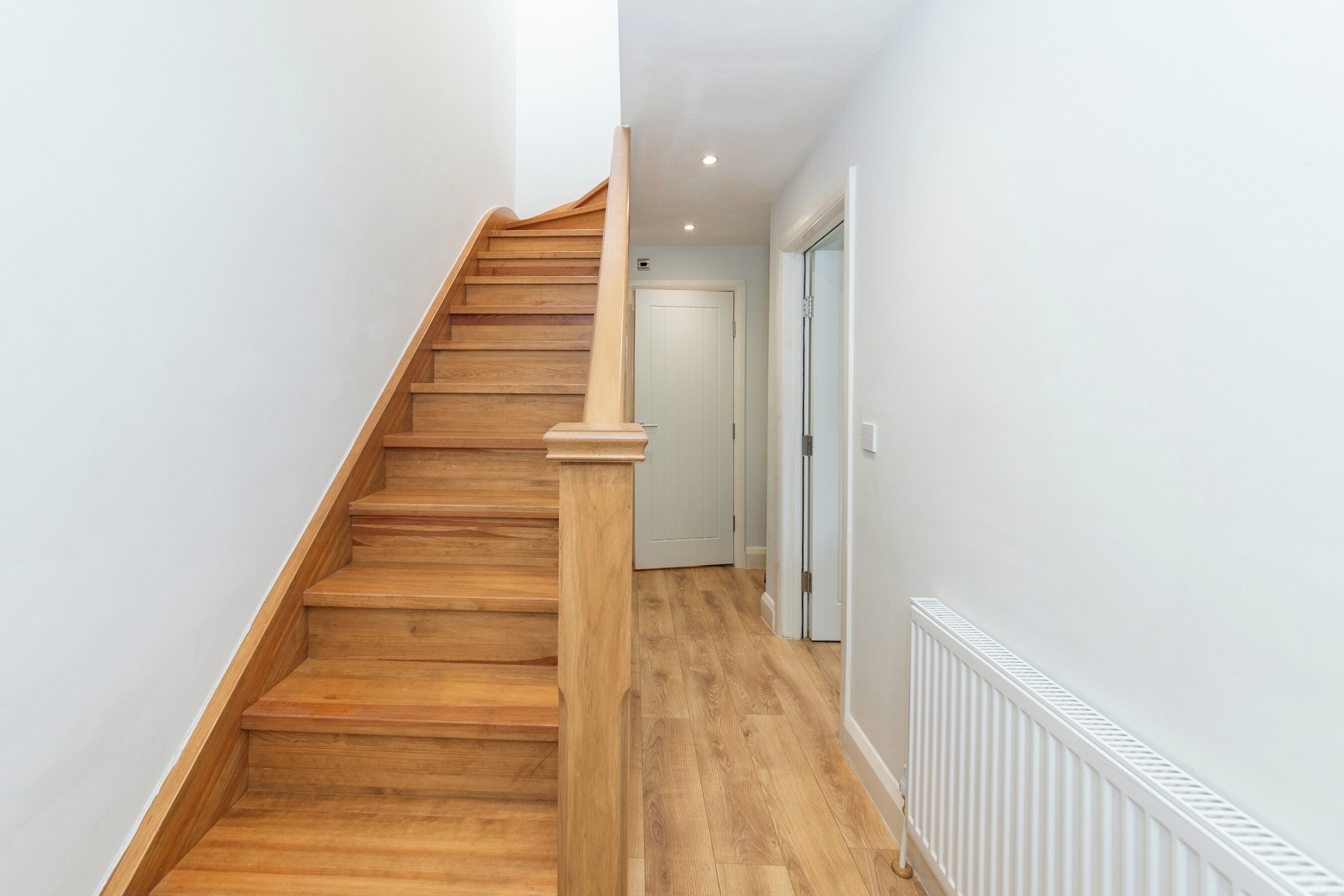 Un escalier en bois avec une rampe, menant à une porte blanche.