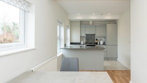 A modern kitchen with a central island, a dining area with a table, and a view of the outdoors. - Duplex Apartment - Modern & Convenient - Pass the Keys (Reading)