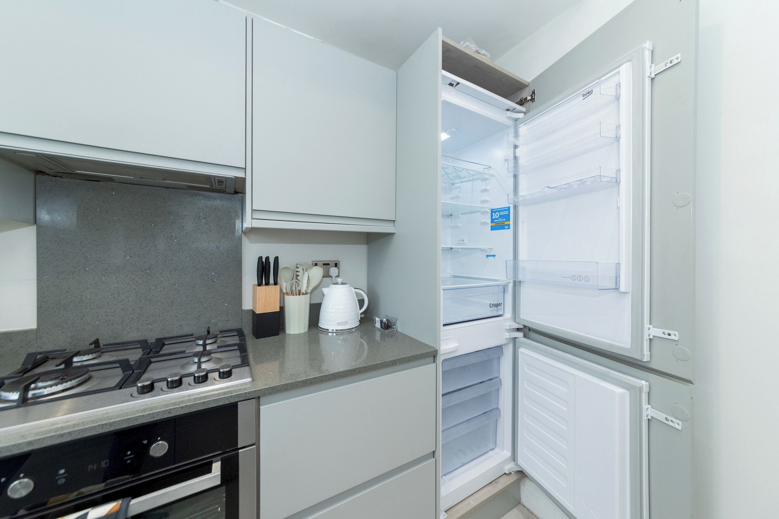 A compact kitchen with a gas stove, a kettle, and a refrigerator.