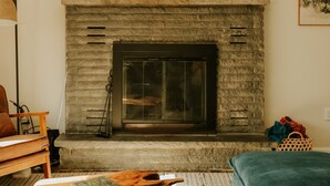Ein gemütliches Wohnzimmer mit Kamin aus Stein, einer hölzernen Bank, einem Tisch mit Büchern und einem blauen Sofa.