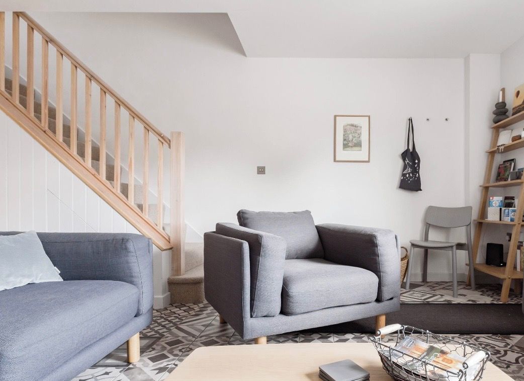 A modern living room with a grey sofa, a wooden staircase, and a bookshelf.