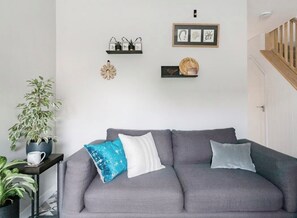 A grey sofa with three cushions, a potted plant, and wall decorations including framed pictures and a decorative piece. - Modern home, sleeps 8, garden
3km from Cambridge, free carpark (Cambridge)