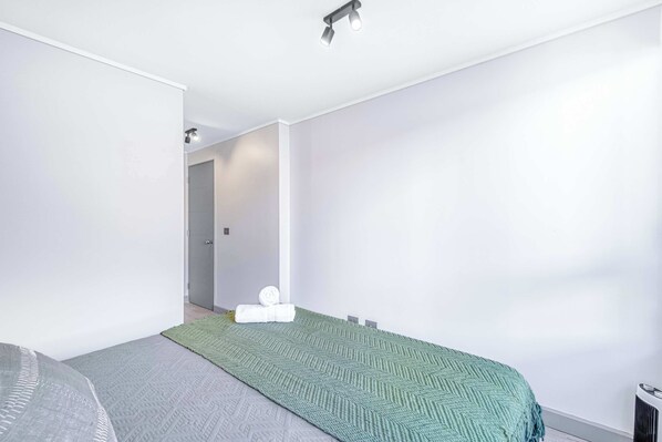 A modern bedroom with a bed, a green textured blanket, and a white wall. - Urban Essence - 2D Santiago (Santiago)