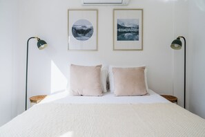 Een netjes opgemaakt bed met twee kussens, twee ingelijste foto's aan de muur en twee vloerlampen aan weerszijden.