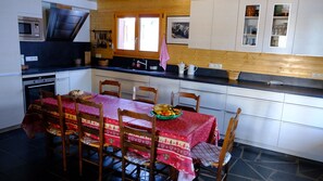 Eine Küche mit Esstisch für sechs Personen, ausgestattet mit Mikrowelle, Backofen und diversen Kochutensilien.
