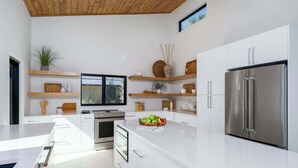 Cozinha moderna com armários brancos, eletrodomésticos de aço inoxidável e prateleiras de madeira.