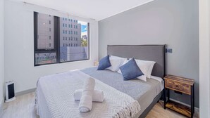 A modern bedroom with a large bed, a view of buildings through a window, and a small bedside table. - Nomad Stay  Pool, Wifi near La Moneda (Santiago)