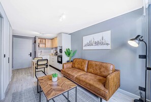 A modern living room with a brown leather sofa, a wooden coffee table, and a cityscape painting on the wall. - Nomad Stay  Pool, Wifi near La Moneda (Santiago)