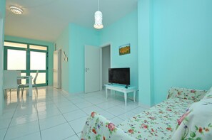 A room with a teal wall, a bed with floral bedding, a TV on a white table, and a door leading to another room. - Semi Dor by BarbarHouse (Torre Suda)