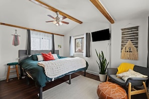 Un dormitorio con una cama, una silla, una planta y un televisor.