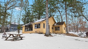 A wooden cabin with a snow-covered roof, surrounded by trees.