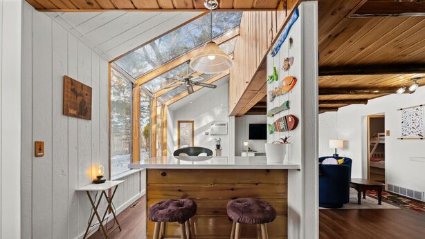 A modern interior with a wooden ceiling, a bar area with stools, and a view through a large window.