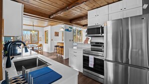 A modern kitchen with stainless steel appliances, wooden ceiling beams, and a large window providing natural light.