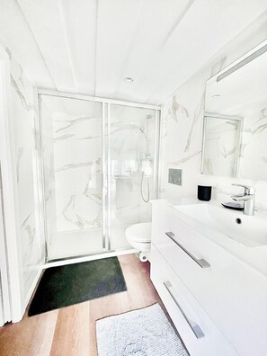 Ein modernes Badezimmer mit Duschkabine aus Glas, einem weißen Waschbecken und einem großen Spiegel.
