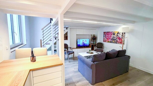 Ein modernes Wohnzimmer mit einer Couch, einem Couchtisch und einem Fernseher. Eine Treppe führt zu einer weiteren Ebene.