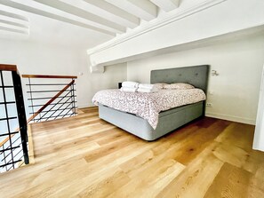 Ein Schlafzimmer mit einem Bett, Holzboden, einer Treppe und einer weißen Decke.