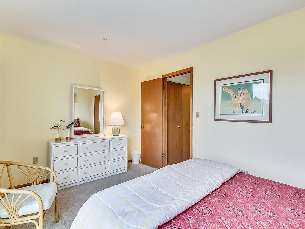 A bedroom with a bed, a dresser, a chair, a wardrobe, and a framed picture on the wall.