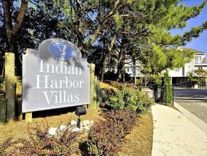 A sign for Indian Harbor Villas with a clear view of the surrounding landscape and a pathway. - Walk to Beach! | 4BR Condo w/ Decks, Views &  BBQ (North Bethany Beach)