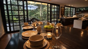 A dining table set with plates, bowls, glasses, and candles, with a view of greenery through large windows. - Candelaria Campestre (El Carmen de Viboral)