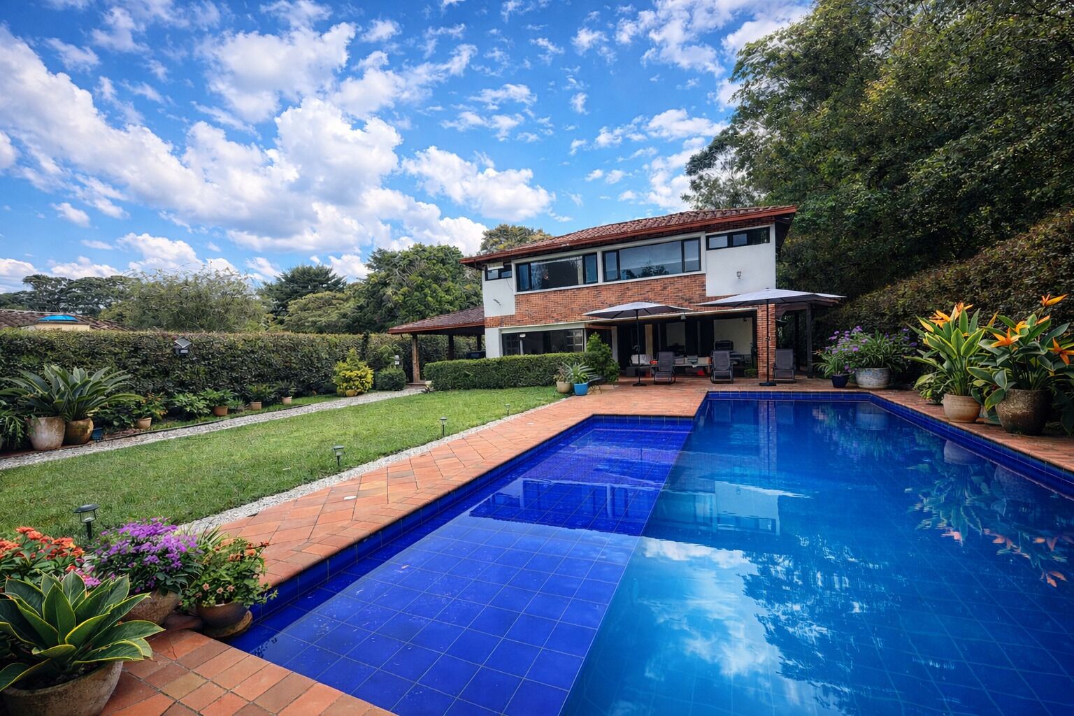 Ein modernes, zweistöckiges Haus mit Swimmingpool, umgeben von üppiger Bepflanzung und Pflanzkübeln.