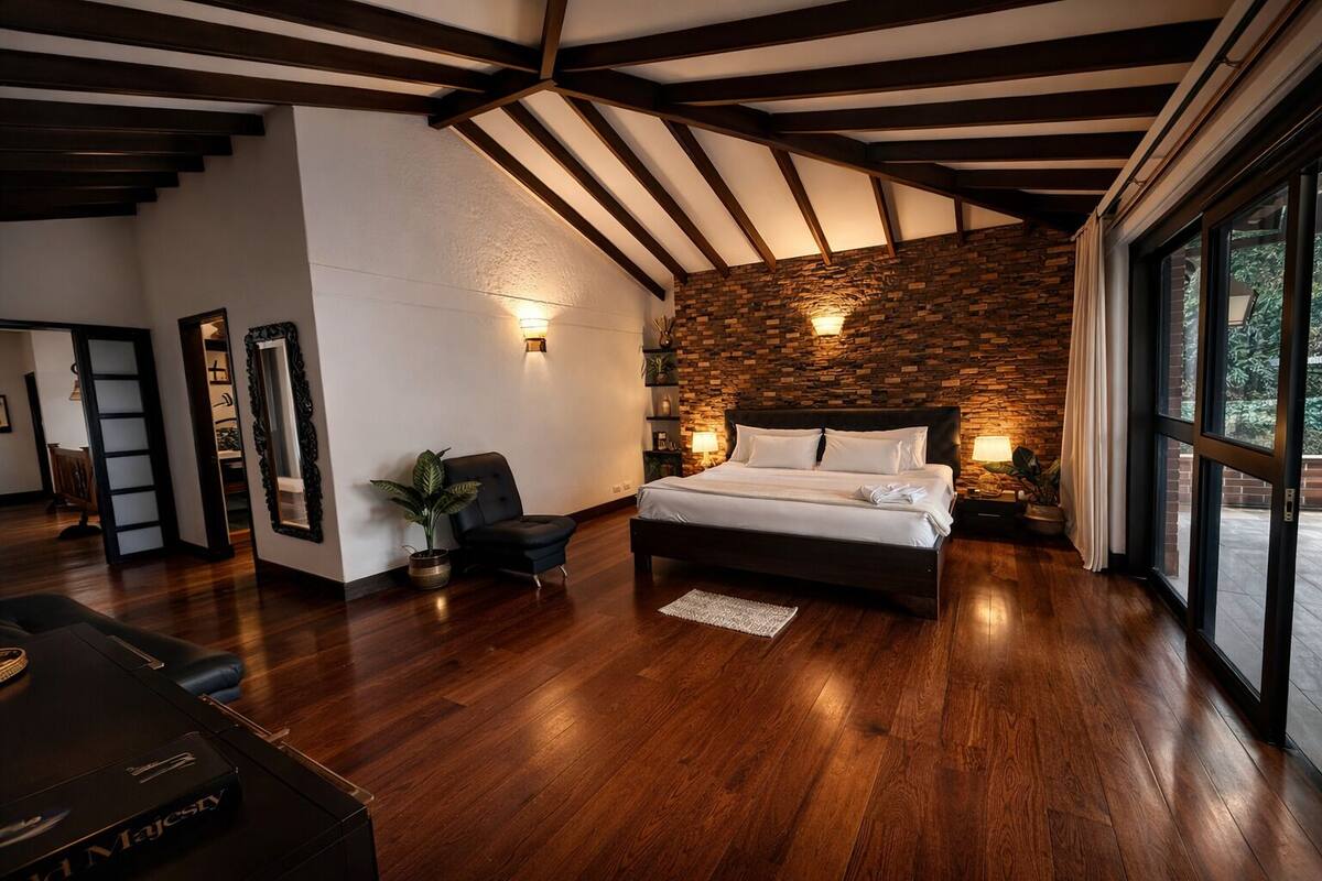 Ein Schlafzimmer mit einem großen Bett, Holzbalken, einer Steinwand und Blick durch große Fenster.