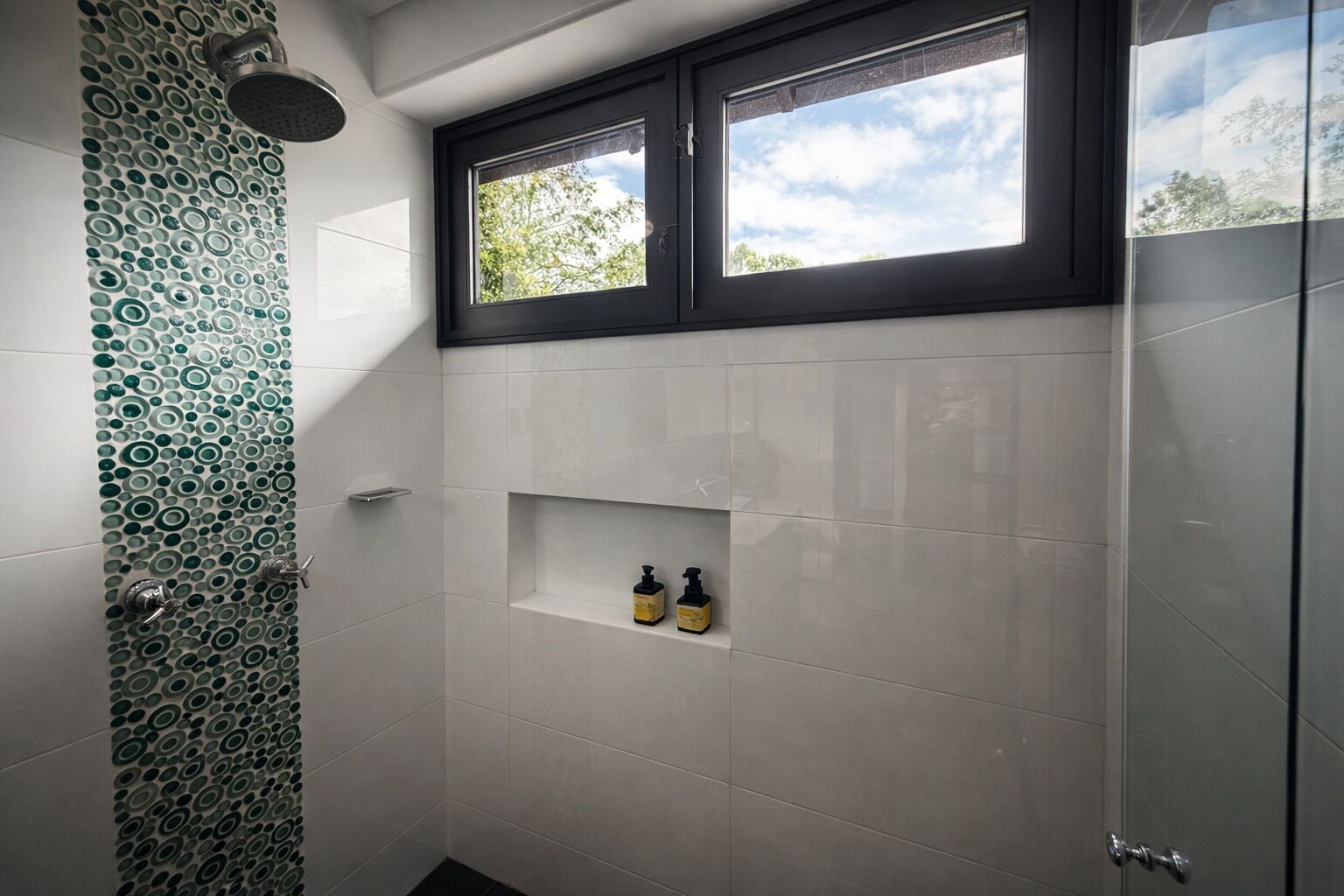 Une salle de bain avec une douche, une fenêtre et une étagère où sont rangés les articles de toilette.