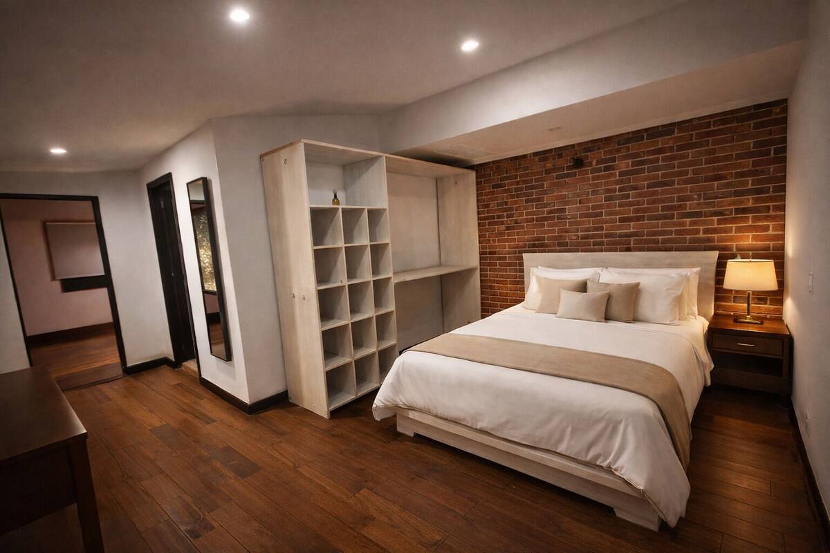 Ein Schlafzimmer mit Bett, Kleiderschrank, Spiegel, Nachttisch und einer Ziegelwand.