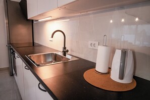 Een moderne keuken met een spoelbak van roestvrij staal, een waterkoker en een keukenrolhouder.