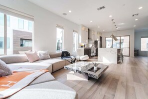 Ein modernes Wohnzimmer mit einer großen Couch, einem Marmortisch und einer Küche im Hintergrund.