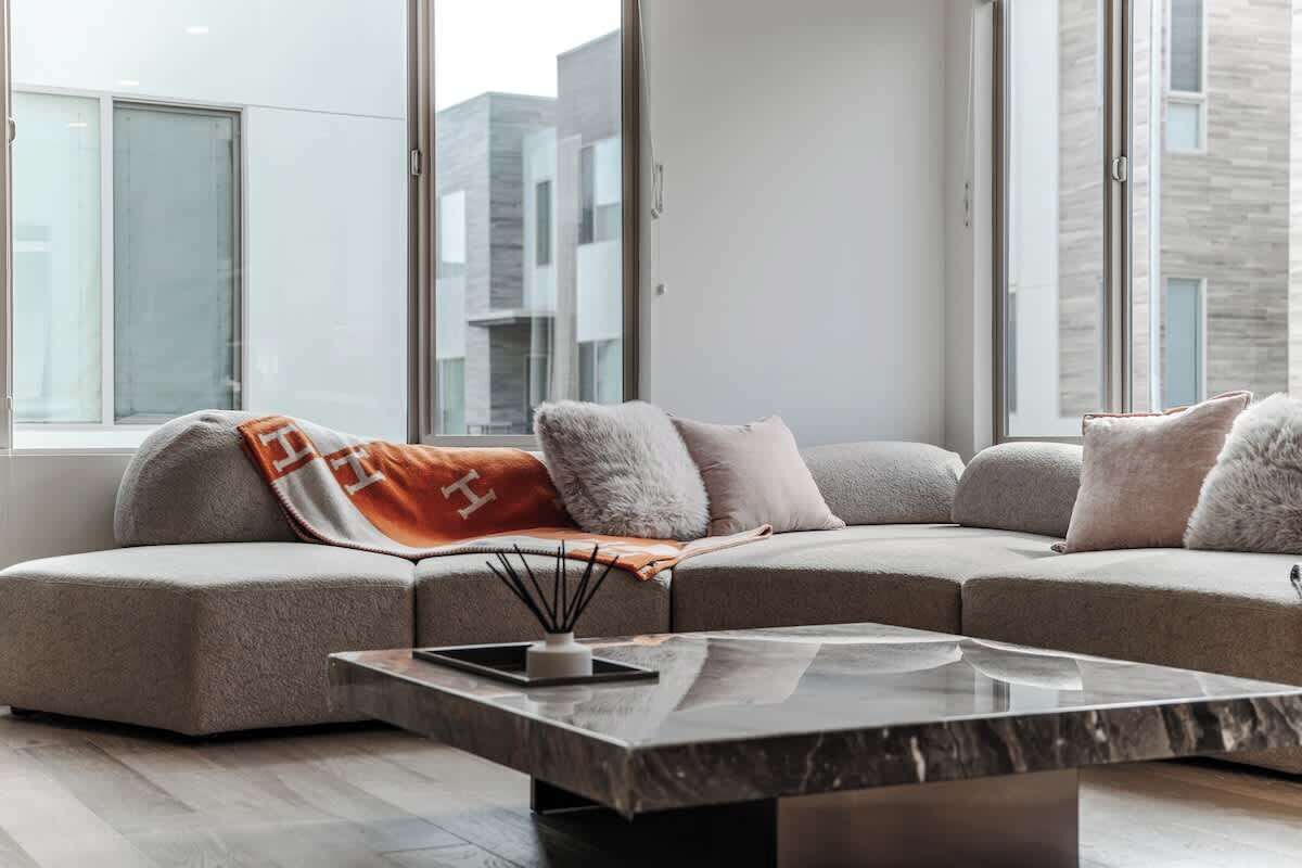 Una sala moderna con un sofá modular, una mesa de centro de mármol y ventanas amplias con vista a la ciudad.