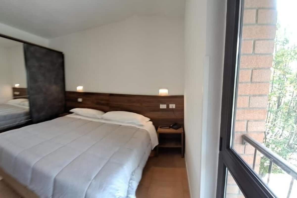 A bedroom with a bed, nightstand, and a large mirror.