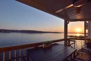 Eine Holzterrasse mit Tisch und Stühlen, mit Blick auf einen stillen See bei Sonnenuntergang.