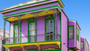 Ein zweistöckiges Gebäude mit einer leuchtend violetten Fassade, grünem Zierrat und einem Balkon mit aufwendigen Metallgeländern.