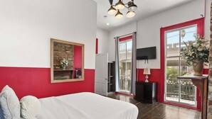 Ein Schlafzimmer mit einem Bett, einem Fernseher, einer rot-weißen Wand, einem Holzboden und einem Balkon mit Geländer.