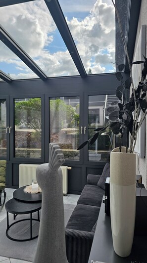 A conservatory with a modern design, featuring a stone sculpture, a large vase, and a sofa. - Eifel Couple Escape - A Getaway for Two: Stylish Apartment with a Sunroom (Reuth)