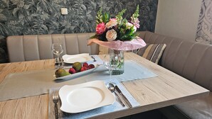 Een gedekte eettafel met borden, bestek, een bloevas en een schaal fruit.