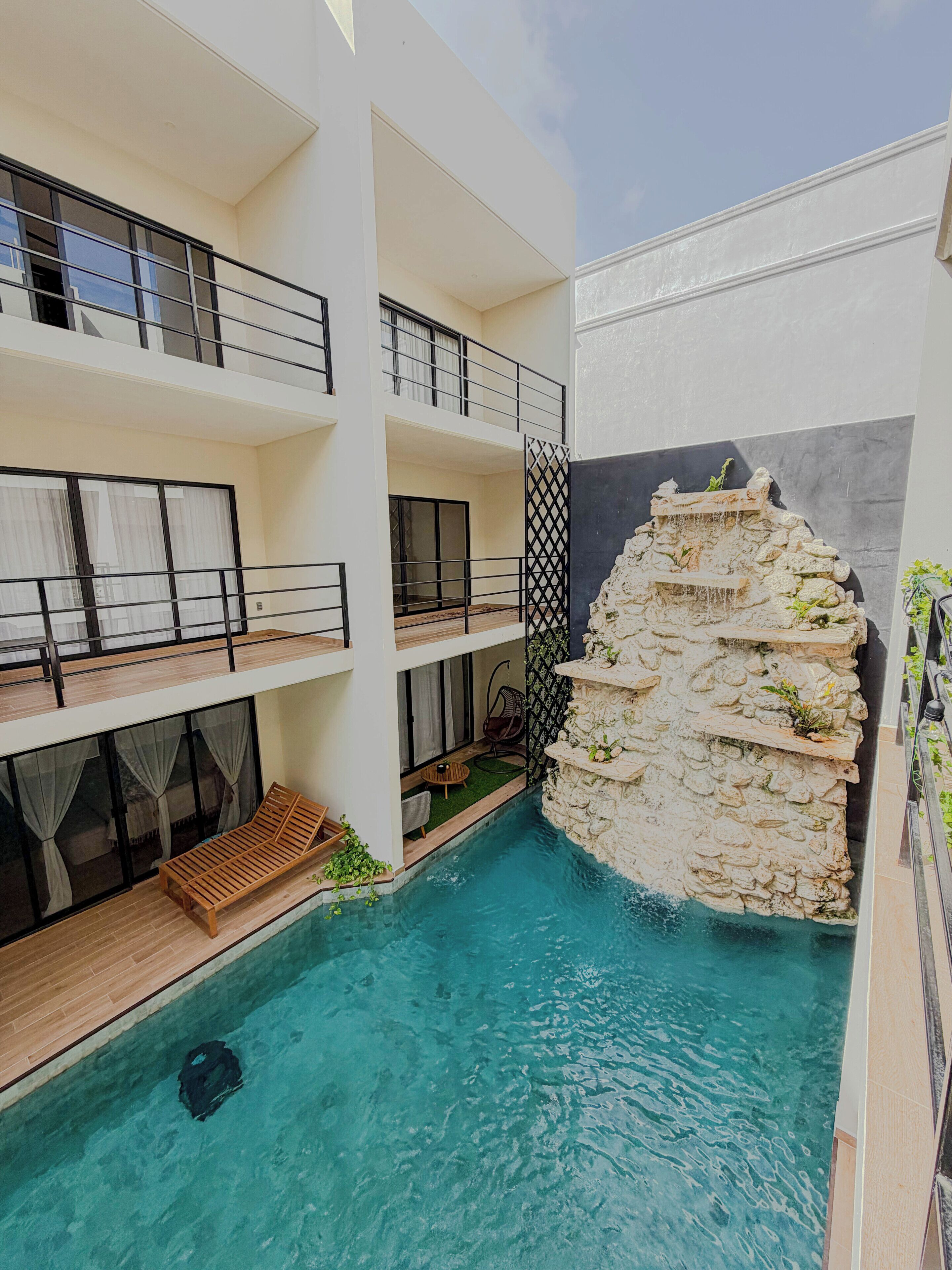 Um hotel com vários andares, piscina central, varandas com grades e uma cascata de pedra.