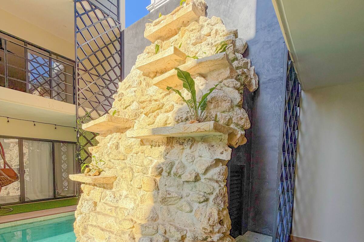 Una fuente de piedra con plantas, una piscina y un balcón con barandilla.