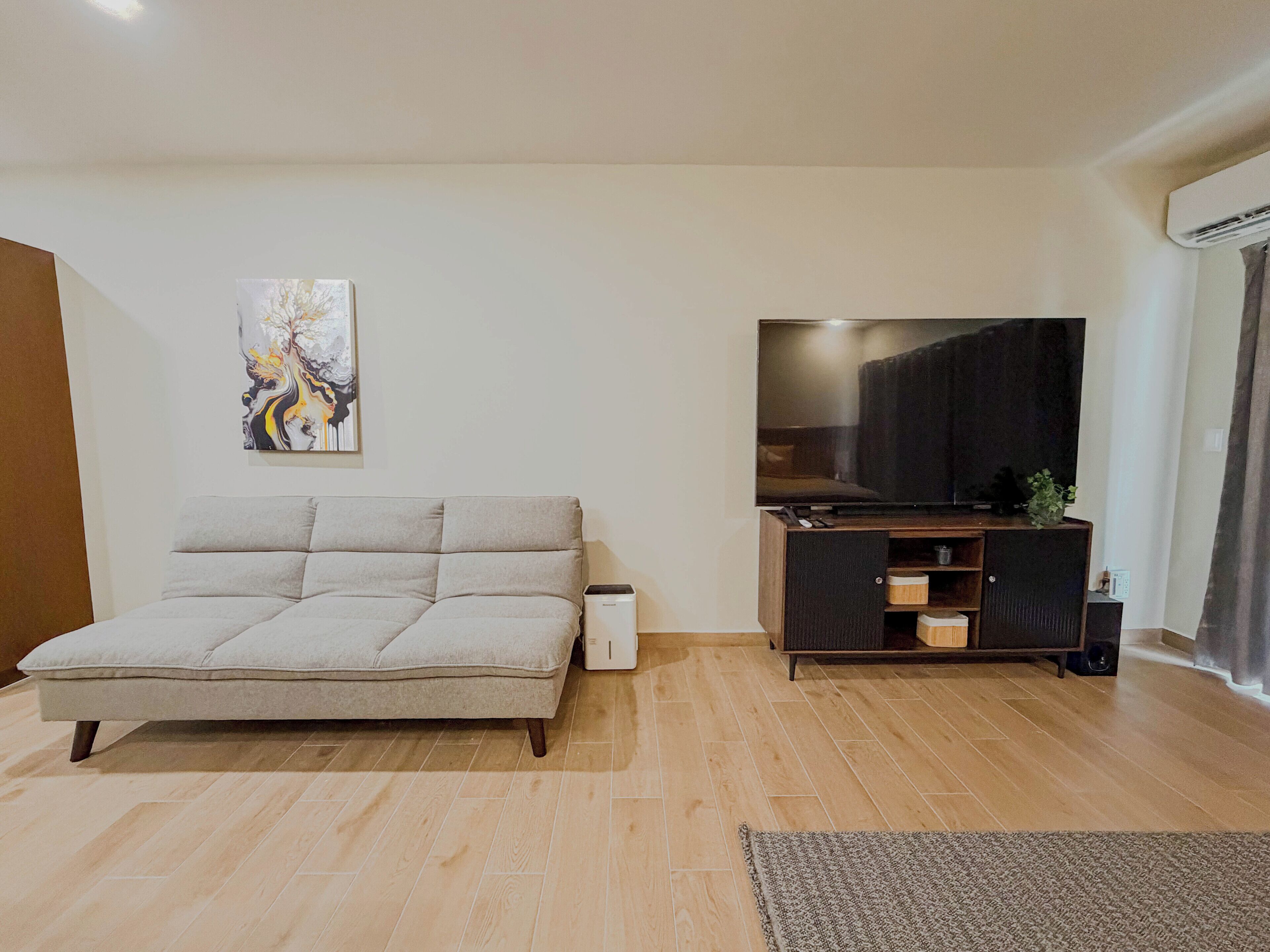 A living room with a sofa, a flat-screen TV, a painting, and a wooden floor.