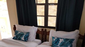 Uma cama de casal com roupa de cama branca e um edredom com padrão de folha tropical azul.