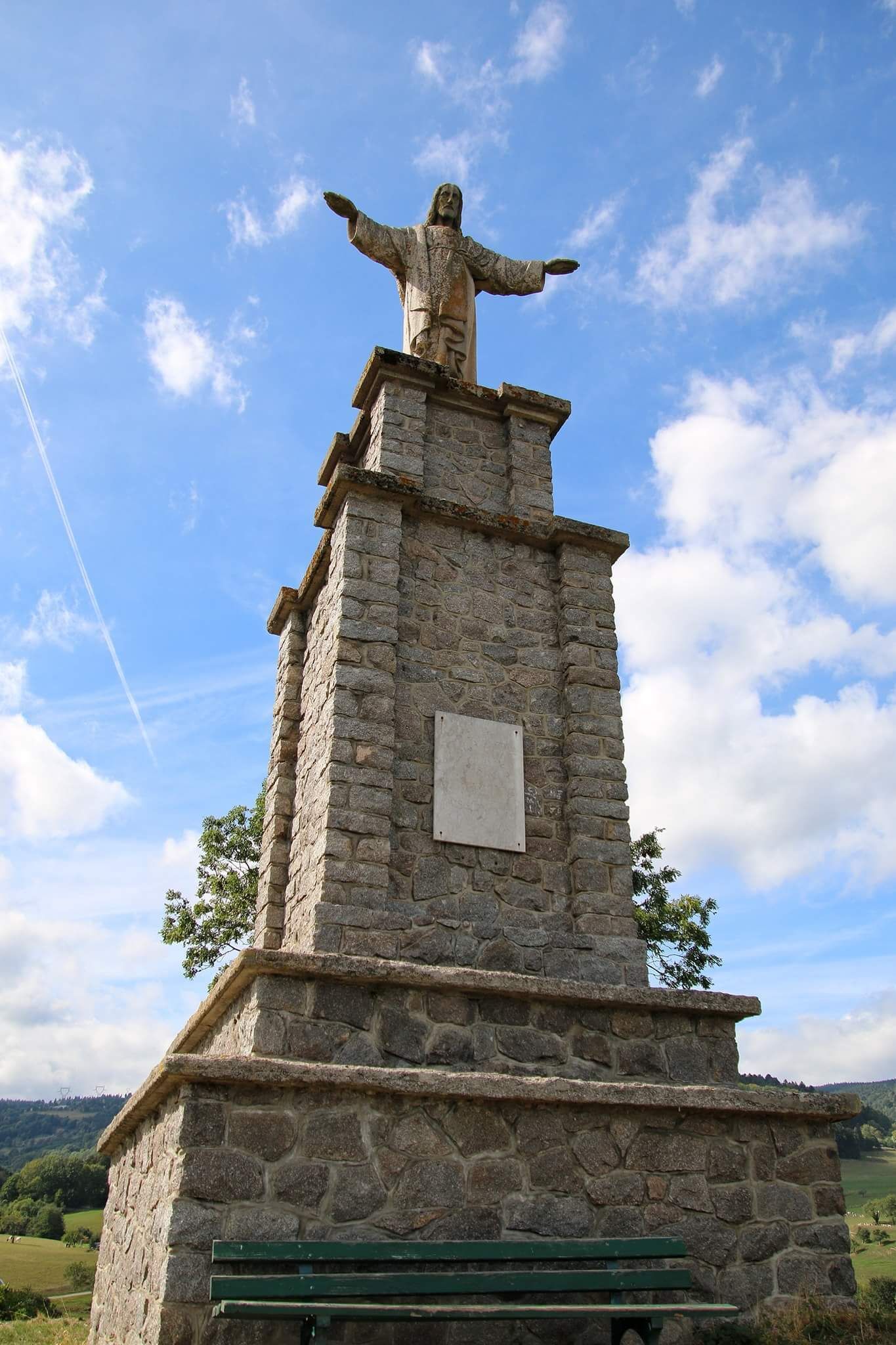 Ett monument av sten med en skulptur, en bänk och en minnesplatta.