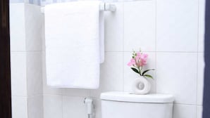 Un baño con inodoro blanco, una toalla blanca colgada en un perchero y una pequeña planta en maceta con flores rosas.